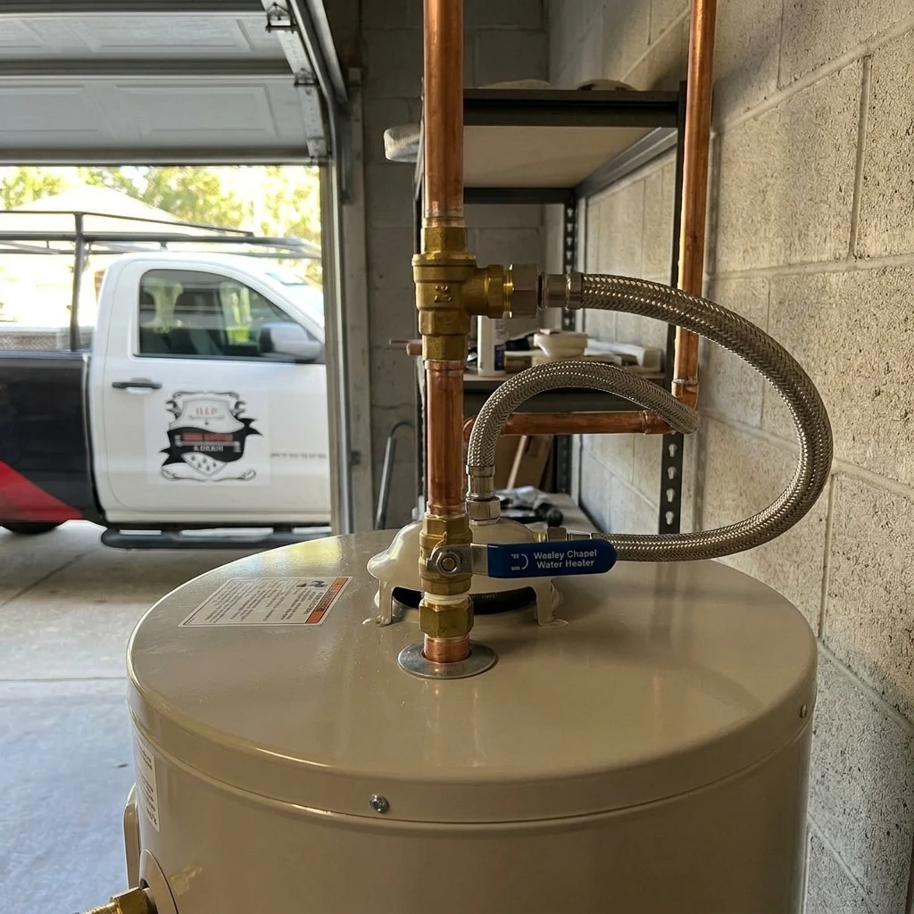 A tank water heater in a garage with copper supply lines and a shutoff valve, the setup in many Valrico homes